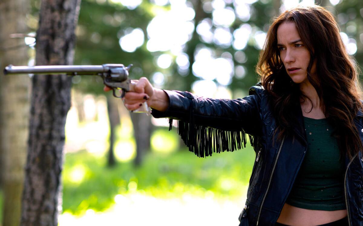 A woman in a fringed jacket aims a long-barreled revolver.