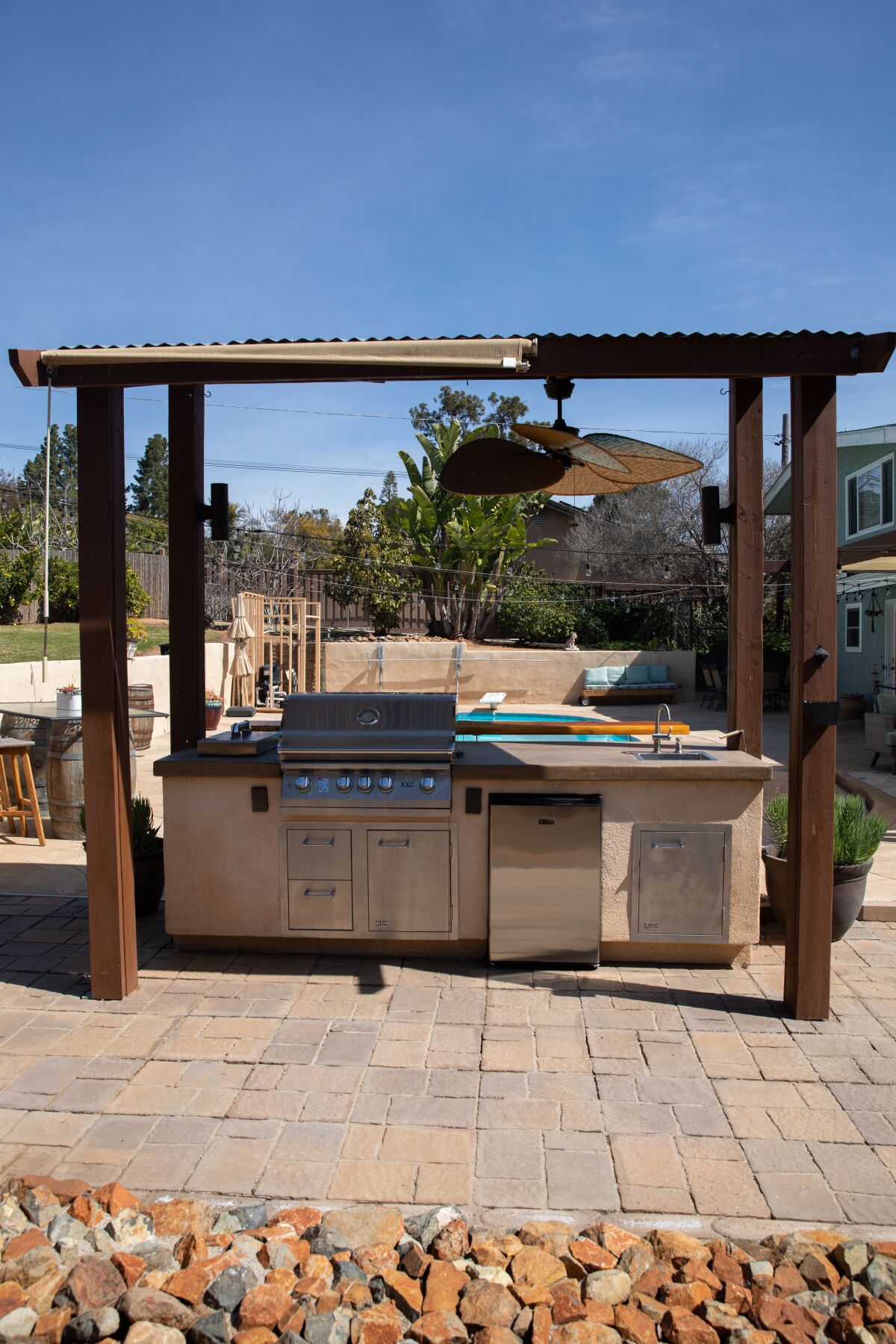 A remodeled outdoor kitchen, showing the side with grill, counter and refrigerator.
