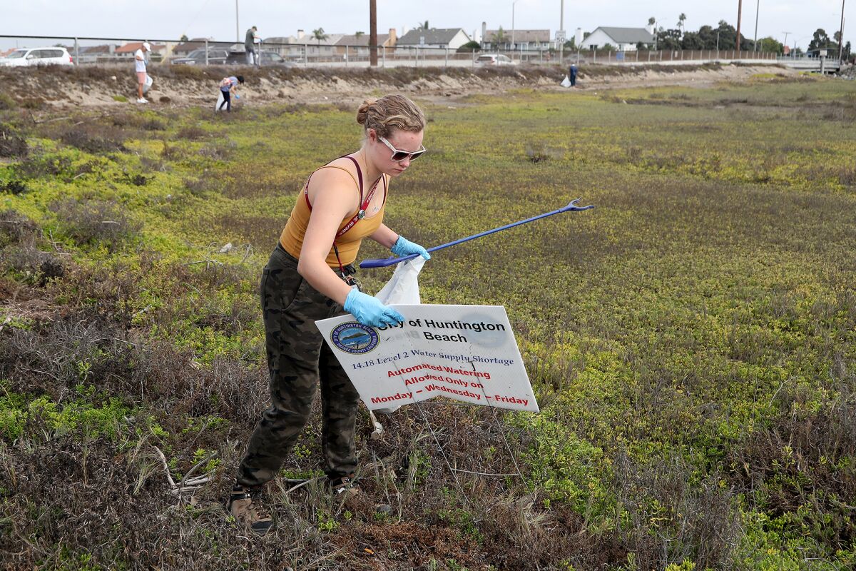 Erika Moe, 22, of Irvine, picks up a sign as she helps remove trash at Talbert Marsh in Huntington Beach on Saturday.