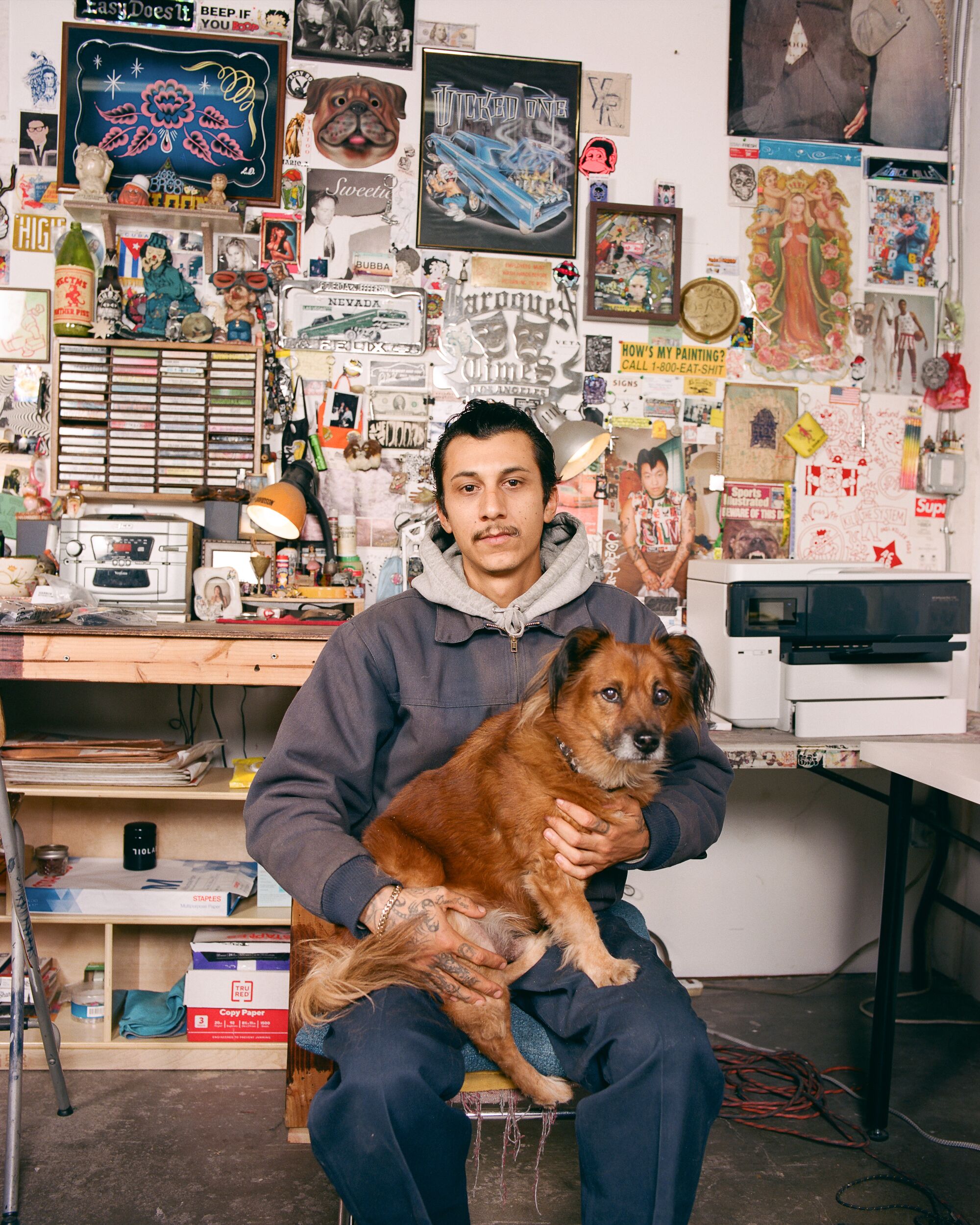 Mario Ayala in his studio with his dog, both looking intently at the camera