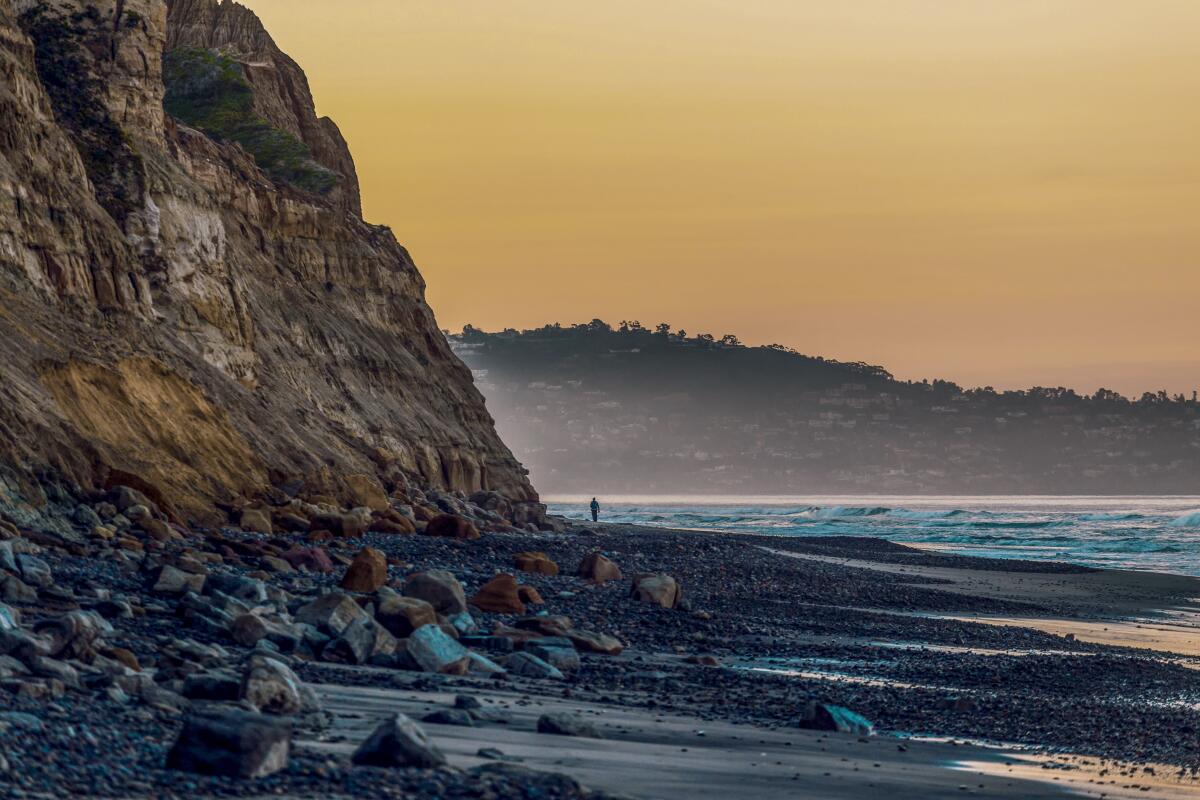 Distant silhouette of a person walking along a rocky beach with cliffs.