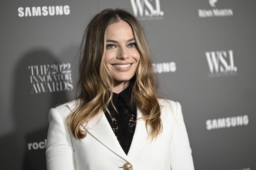 A woman with long hair wears a white blazer and dark shirt and smiles upon arrival at an event