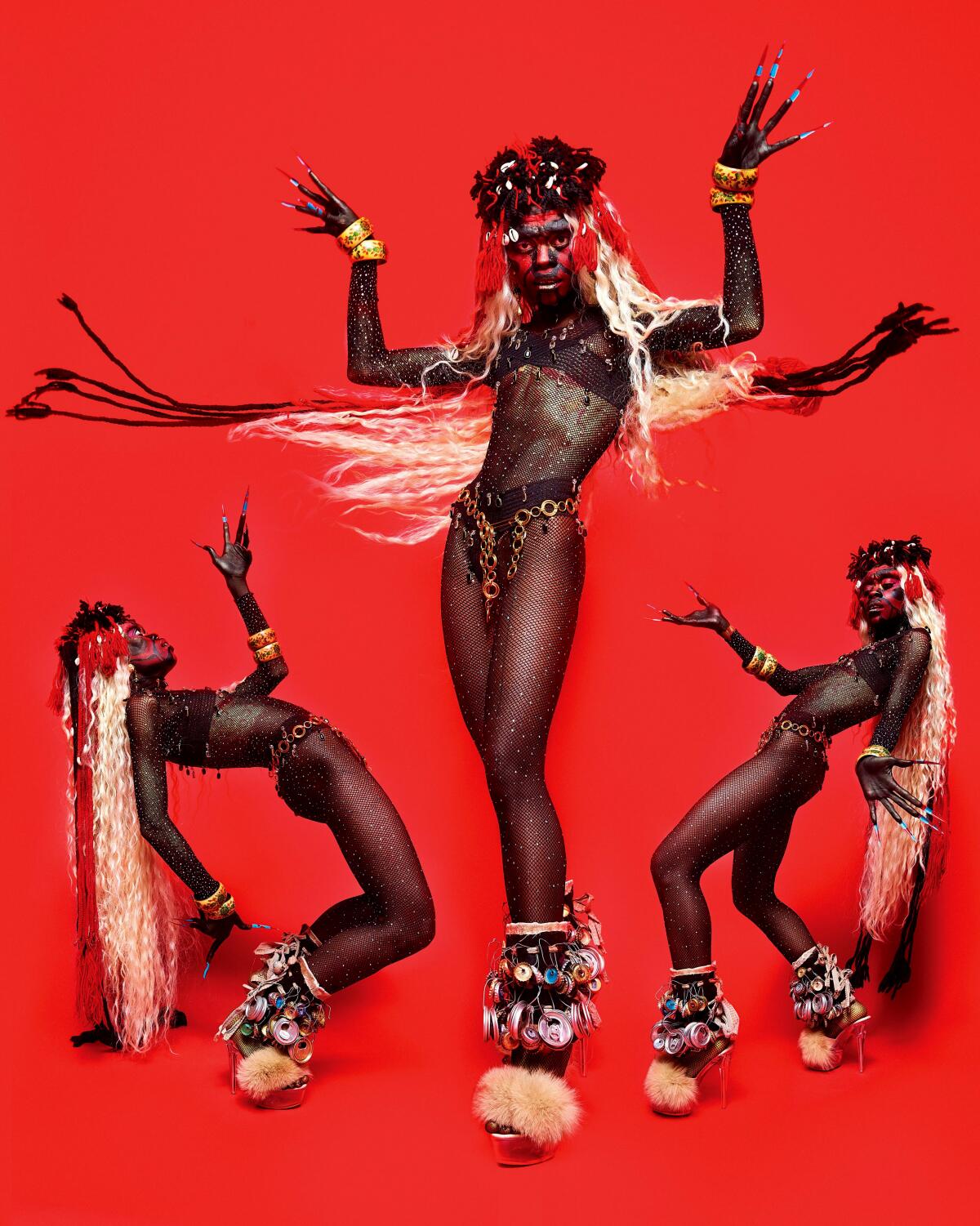 Three nearly naked people pose in front of a bright red background with long, multi-colored hair.