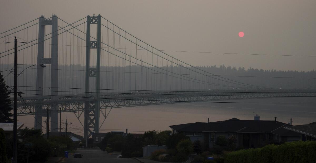 One end of twin suspension bridges over a body of water on a gray day 