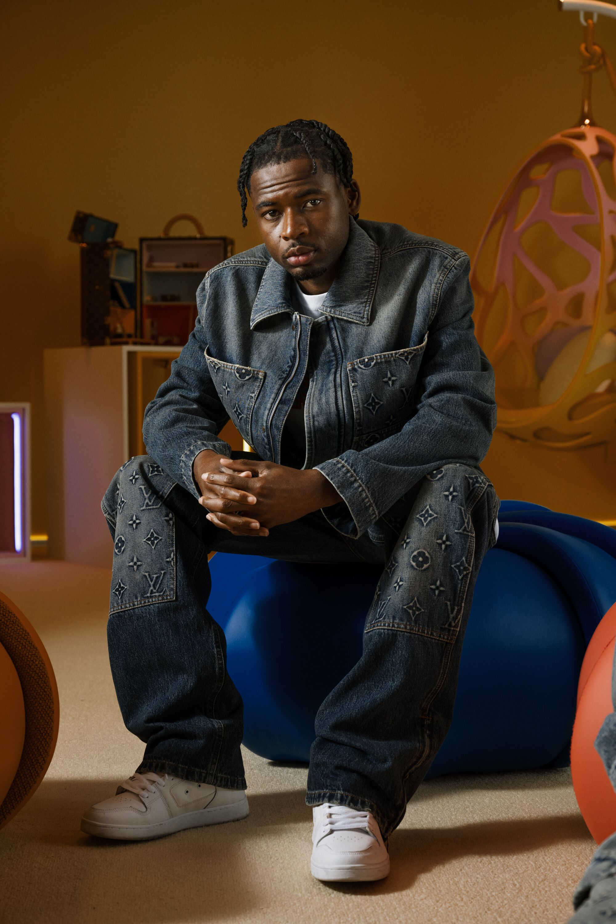 A man wearing denim sits on a blue pouf.