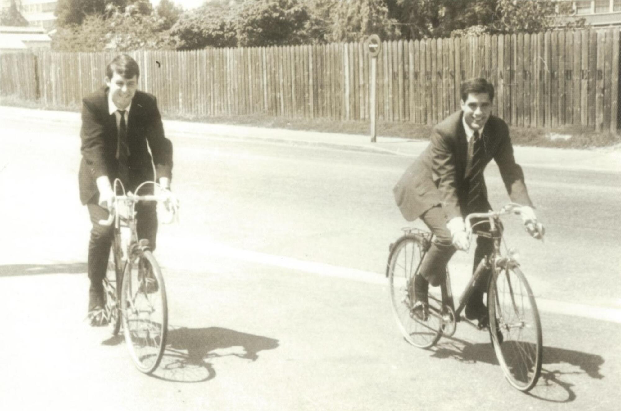 Romney, right, on a bike in France wearing a suit and tie.