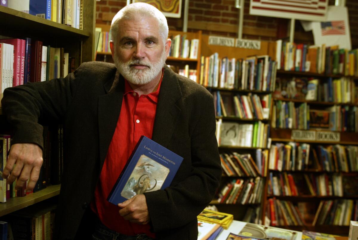 A man holds a book in front of bookcases.
