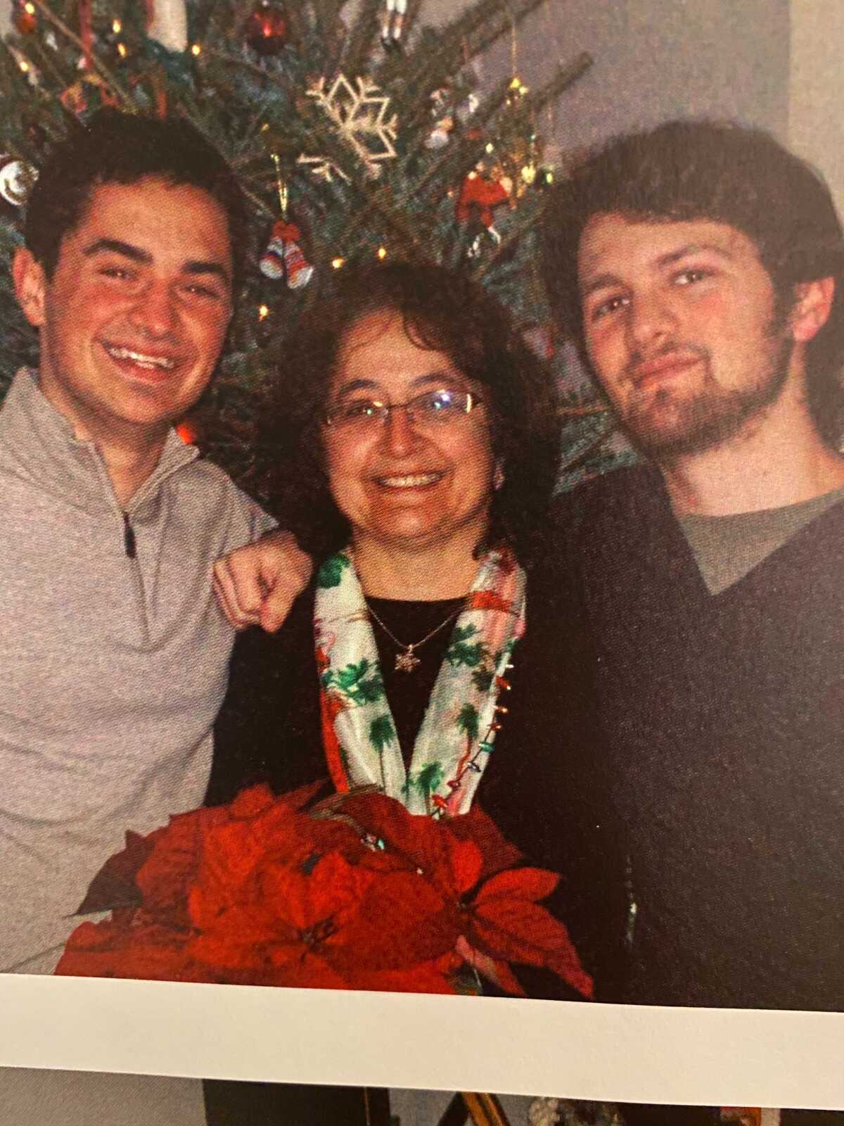 A family photo of a mother and her two adult sons in front of a Christmas tree