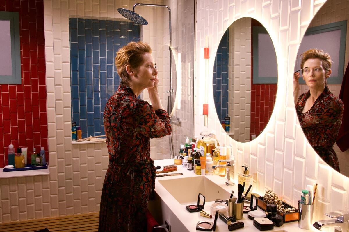 Tilda Swinton, in "The Human Voice," applies makeup at a mirror in a cluttered bathroom.