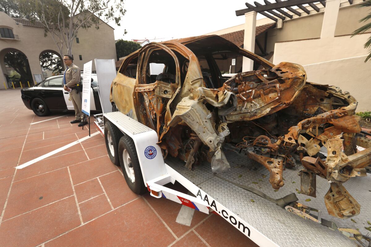 A crashed, crushed, burned-out shell of a car sits on a trailer.