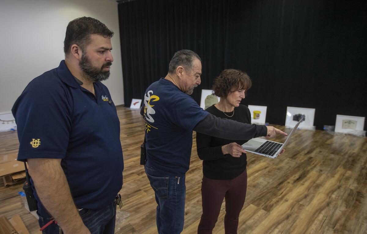 Lorene Delany-Ullman gives instructions Monday to UC Irvine staff members Sal Aduna, left, and Alex Nava on how to install an exhibit called "Saved: Objects of the Dead." The display opened Tuesday and continues through Feb. 17.