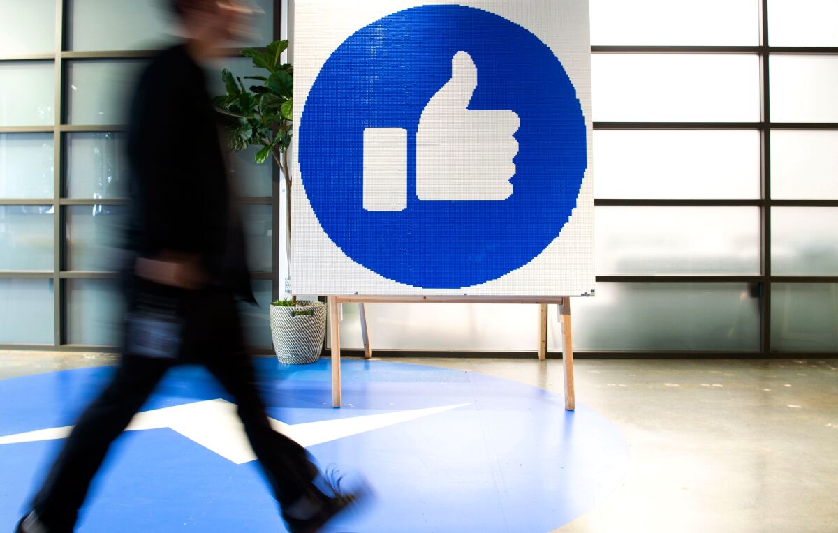An employee walks by a sign displaying the "like" sign at Facebook's corporate headquarters