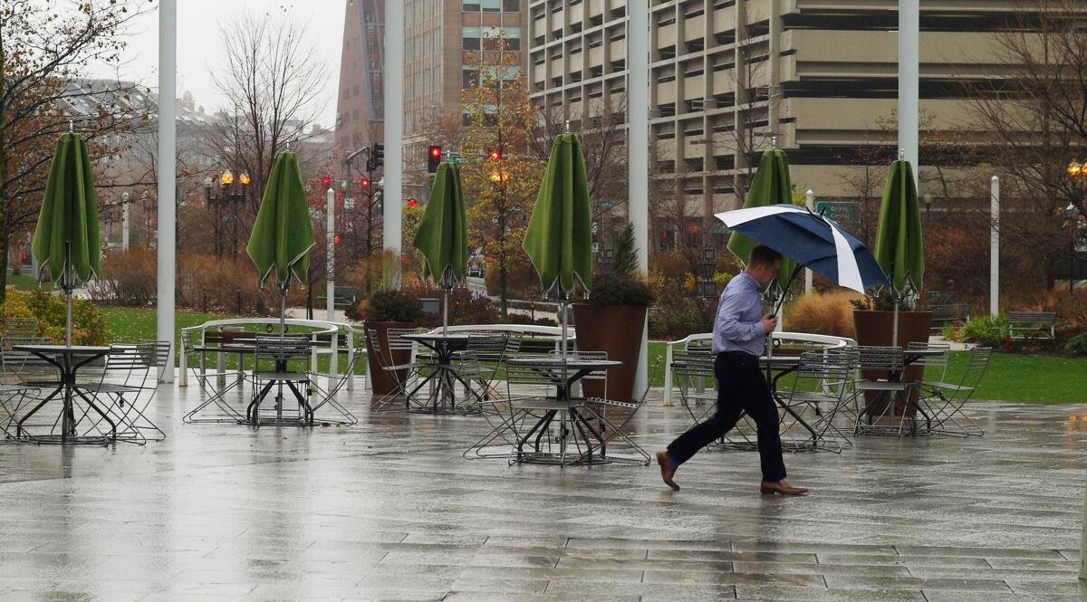 A pedestrian sheltering under an umbrella walks past empty outdoor seating on the Rose Kennedy Greenway in Boston on Monday. Cold temperatures and a storm are predicted due for the upcoming holiday travel days.
