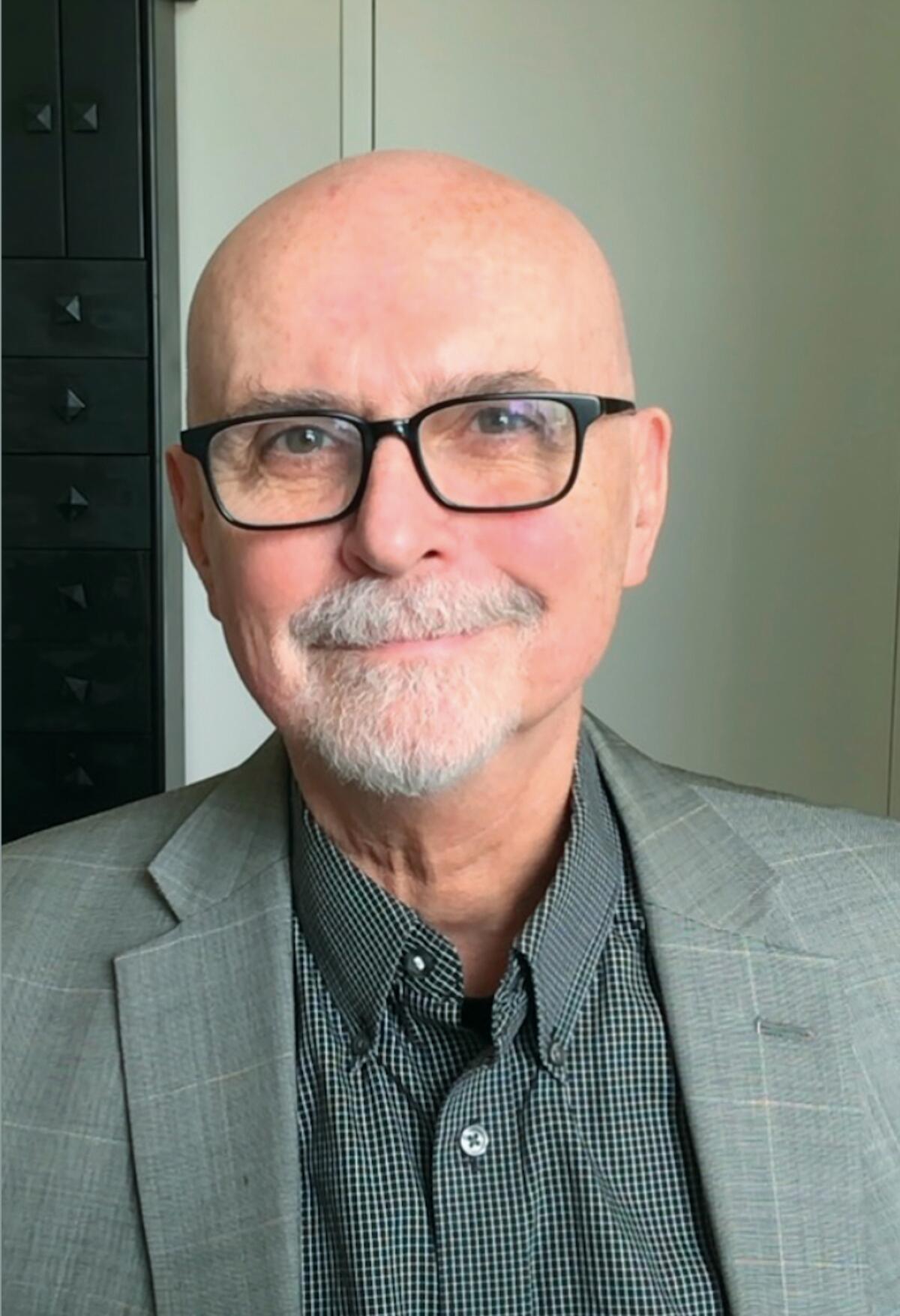 A photograph of a smiling man with a gray suit, dark glasses and a mustache and goatee.