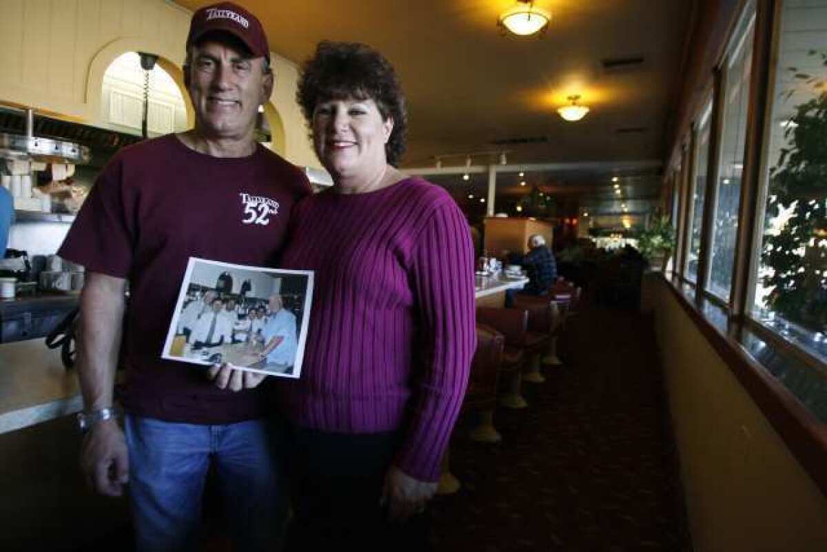 Mark Thomas, from left, and his sister, Karen Ross, pose with a photo of Huell Howser in their Burbank restaurant, Tallyrand.
