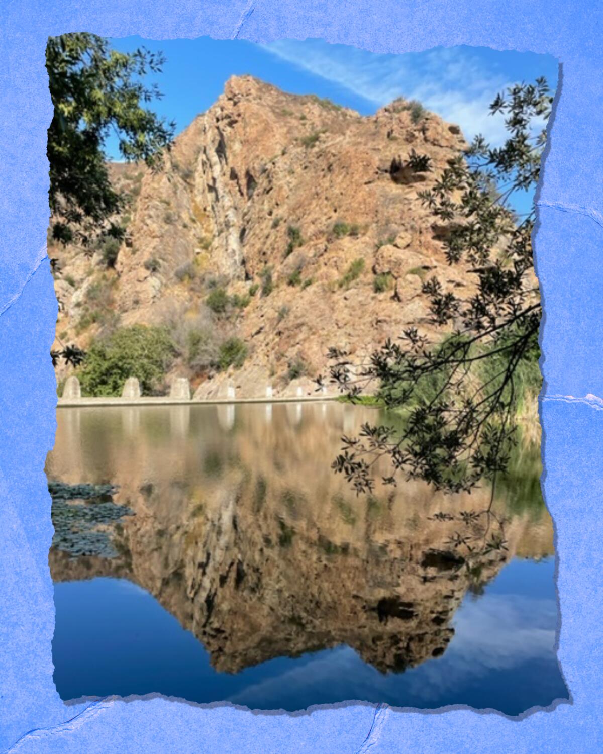 A jagged hill is reflected in a still body of water.