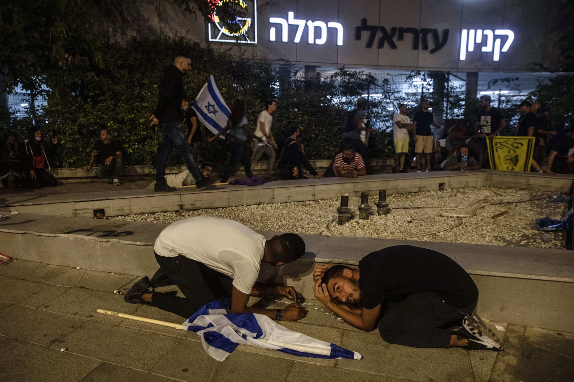 People, some with Israeli flags, take cover while others remain standing nearby