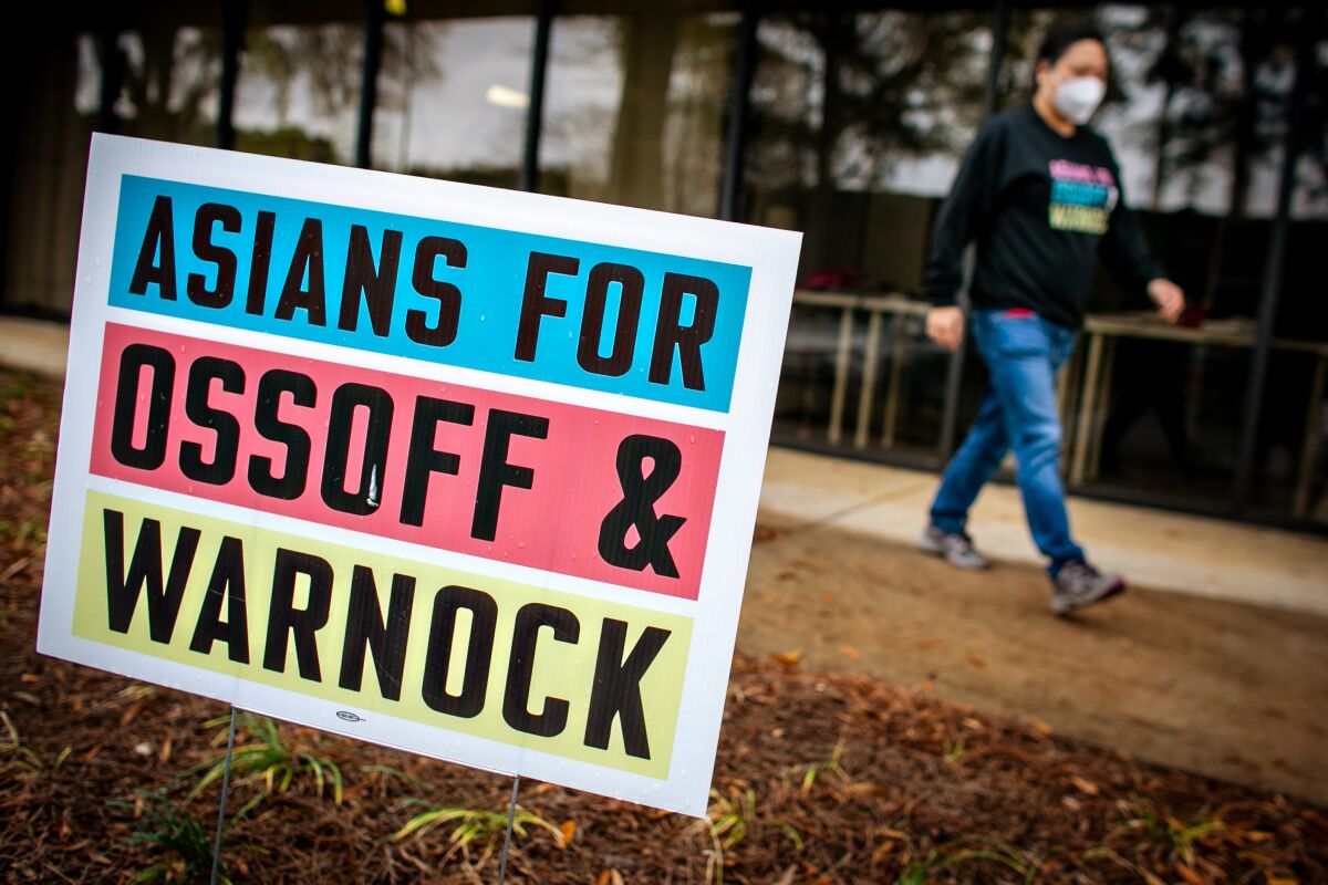 A person walks along a sidewalk past a yard sign that reads "Asians for Ossoff & Warnock."