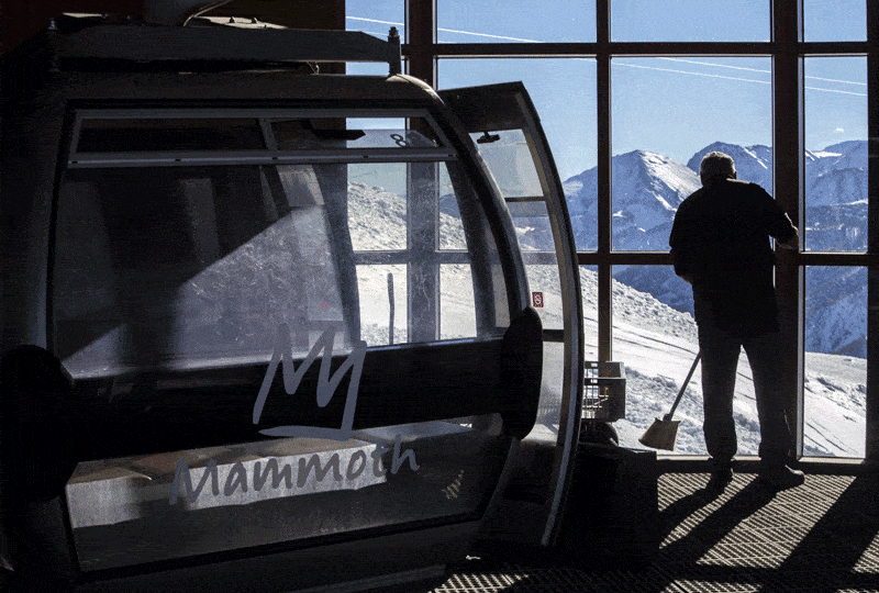 A person sweeps in front of a wall of windows. Outside are snowy mountains.