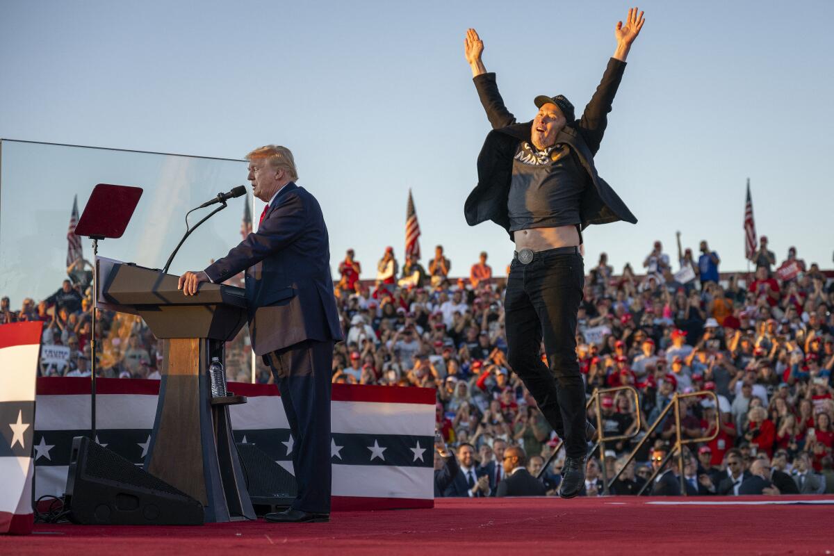 A man in a suit speaks at a lectern with a clear shield, left, as another man jumps up in the air with arms raised