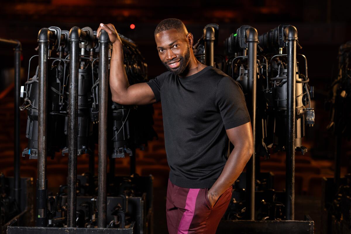 Tarell Alvin McCraney, in a dark T-shirt and striped pants, stands amid props on a stage.