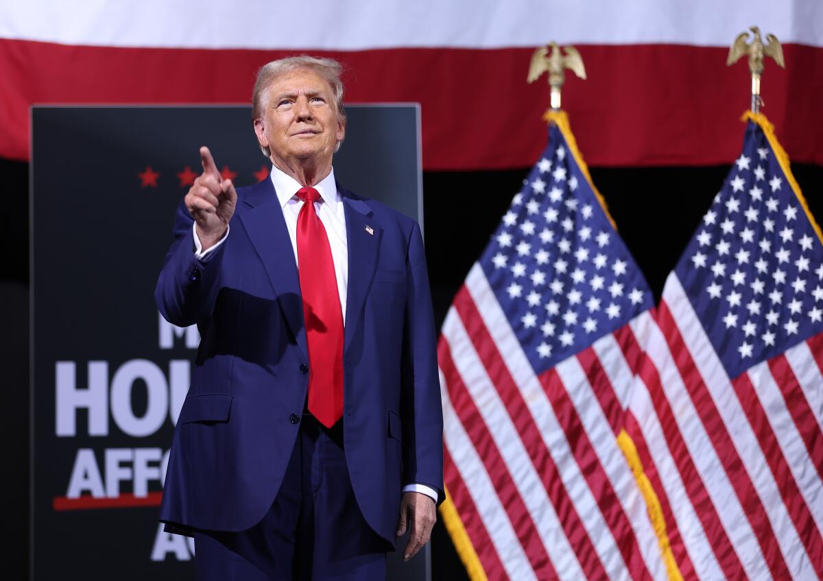 Donald Trump points an index finger as he stands next to two U.S. flags