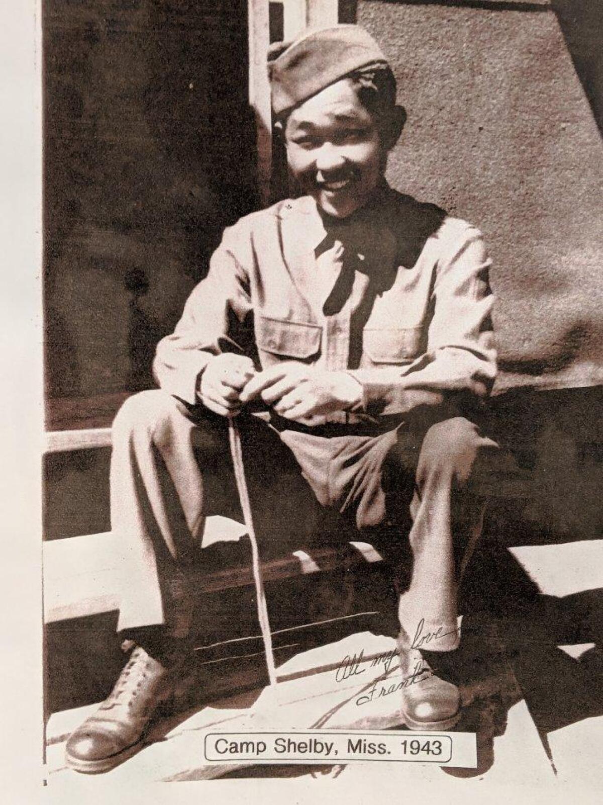 In a black-and-white photo, young Frank Wada sits on a step in his military uniform.