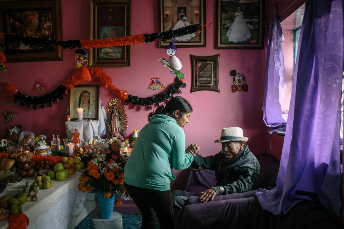 Nayeli Hacinto gently helps up her grandfather, Antonio Alvarado Casas, 87, from his quiet contemplation of their family Day of the Dead alter in Metepec, Puebla. Alvarado has lived in the town nearly his whole life, working in a local factory to support his family.