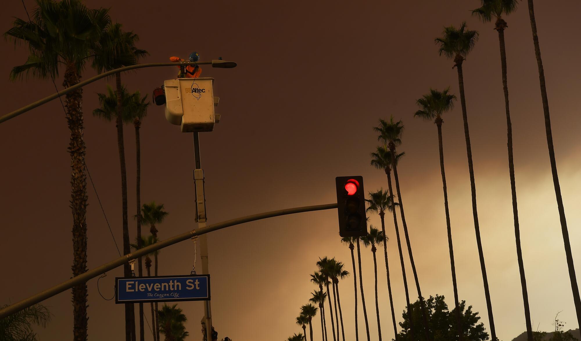 A worker installs a street camera to a light post in Azusa on Wednesday as smoke covers the sky from the Bobcat fire.