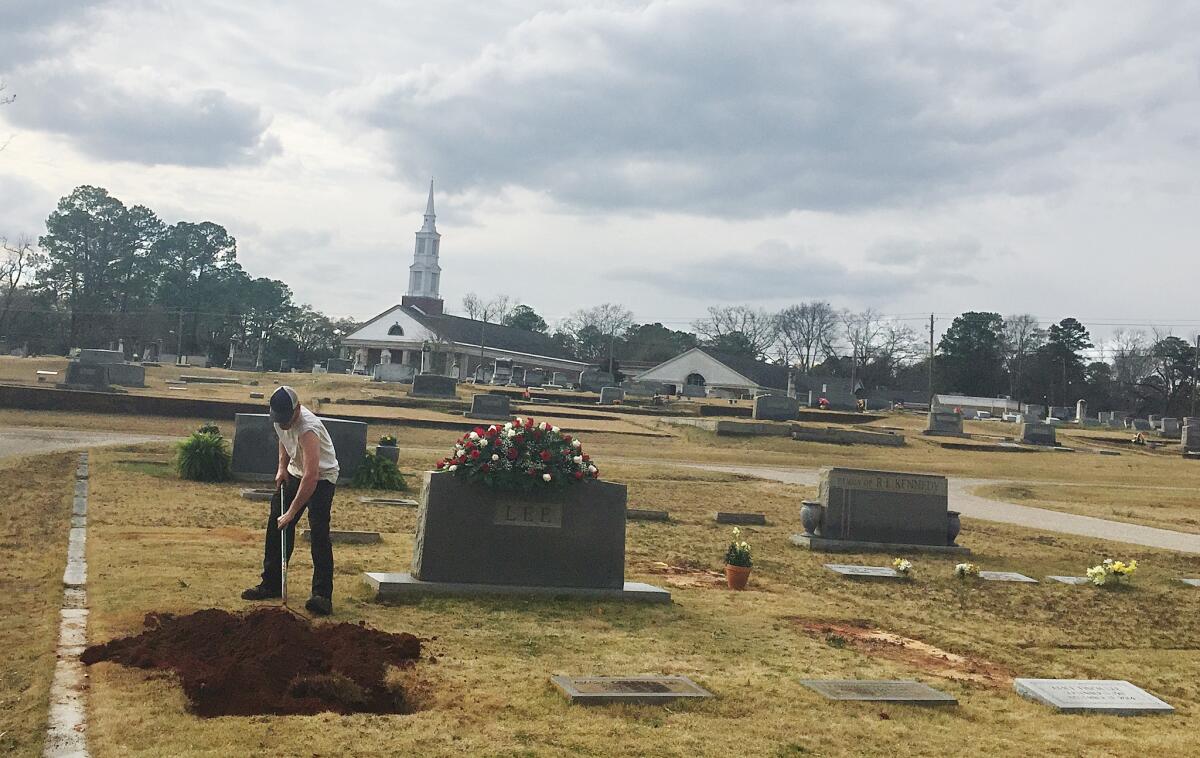 A man rakes dirt over a grave in the Lee family cemetery plot Saturday in Monroeville, Ala.