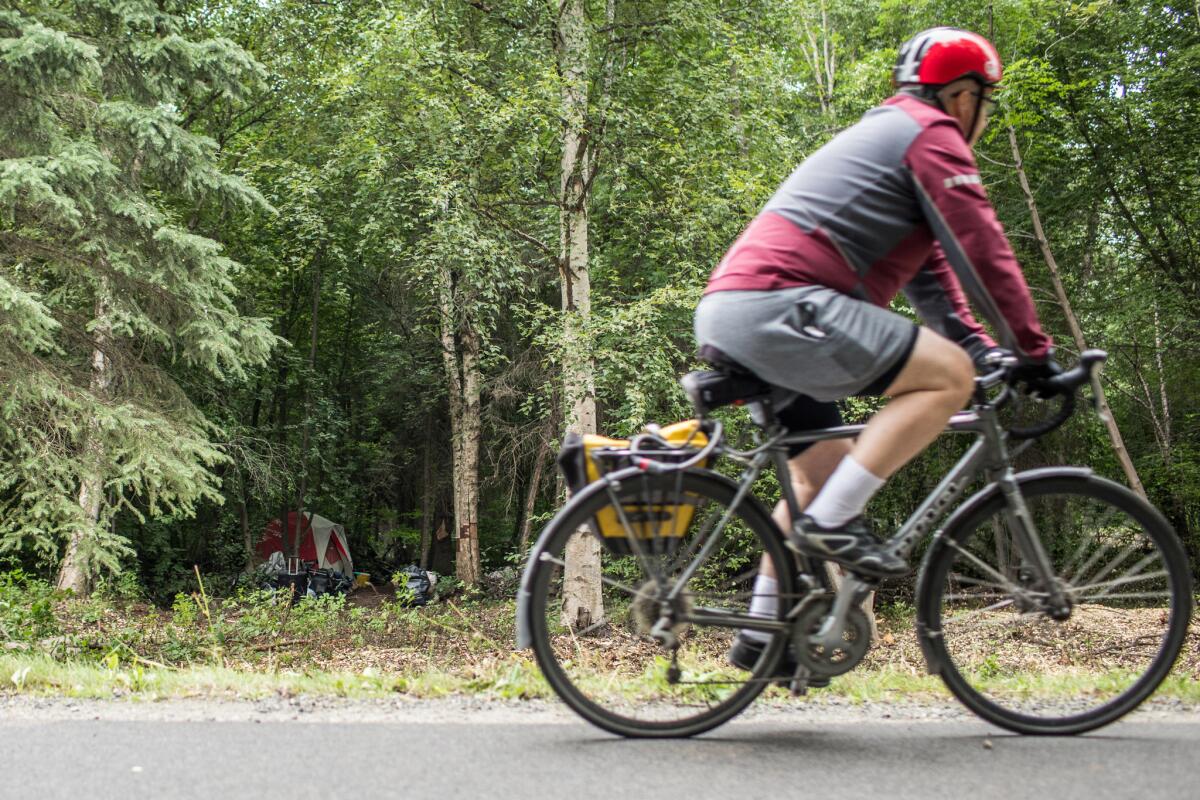 A bicyclist passes a homeless camp set up along the Chester Creek Trail in Anchorage.