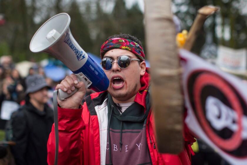 In this Saturday, April 7, 2018, photo, Cedar George-Parker addresses the crowd as protesters opposed to Kinder Morgan's plan on Trans Mountain pipeline extension, in Burnaby, British Columbia. Kinder Morgan is suspending all non-essential activities and related spending on the Trans Mountain pipeline expansion project. (Darryl Dyck/The Canadian Press via AP)
