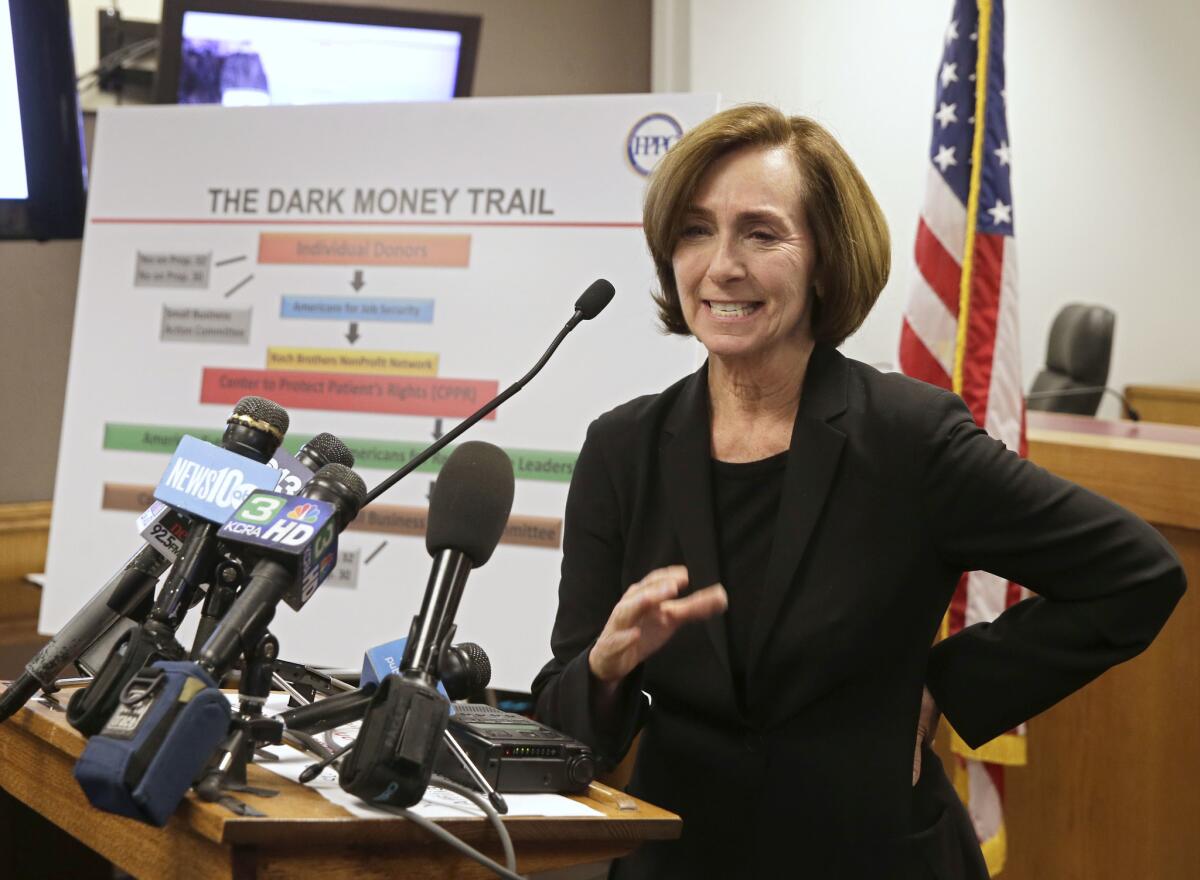 Ann Ravel stands at a lectern. Behind her is a poster with the title "The Dark Money Trail."