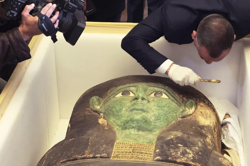 Mostafa Waziri, top official at the Supreme Council of Antiquities, takes a look with a magnifier at an ancient wooden sarcophagus during a handover ceremony at the foreign ministry in Cairo, Egypt, Monday, Jan. 2, 2023. An ancient wooden sarcophagus that was featured at the Houston Museum of Natural Sciences was returned to Egypt after U.S. authorities determined it was looted years ago, Egyptian officials said Monday. (AP Photo/Mohamed Salah)