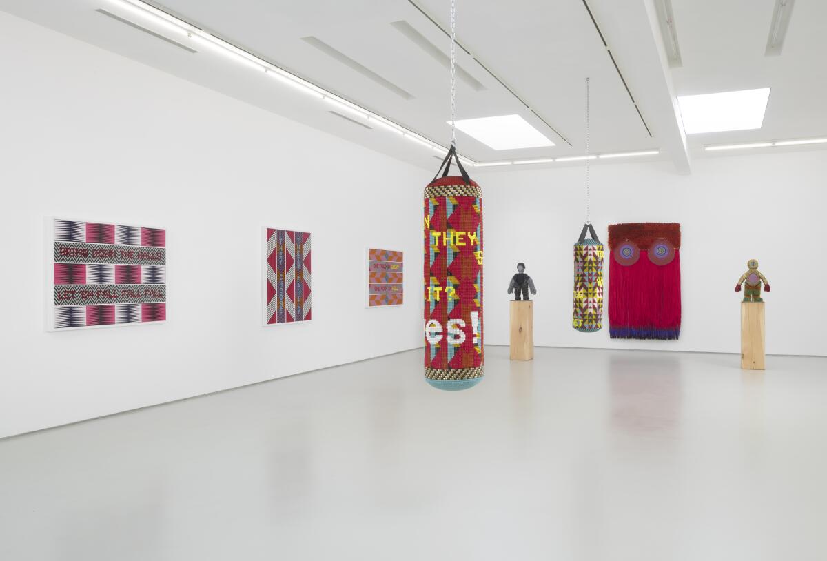 A wide view of a gallery shows a beaded punching bag and abstract, geometric works on the walls.
