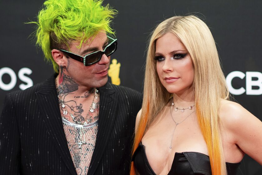 A man with short green hair and a woman with long blond hair posing together in formalwear