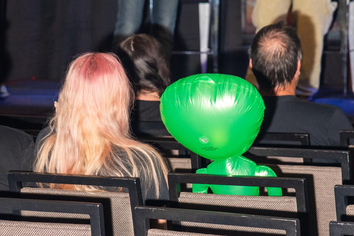 A woman listens to the lecture next to an inflatable alien.