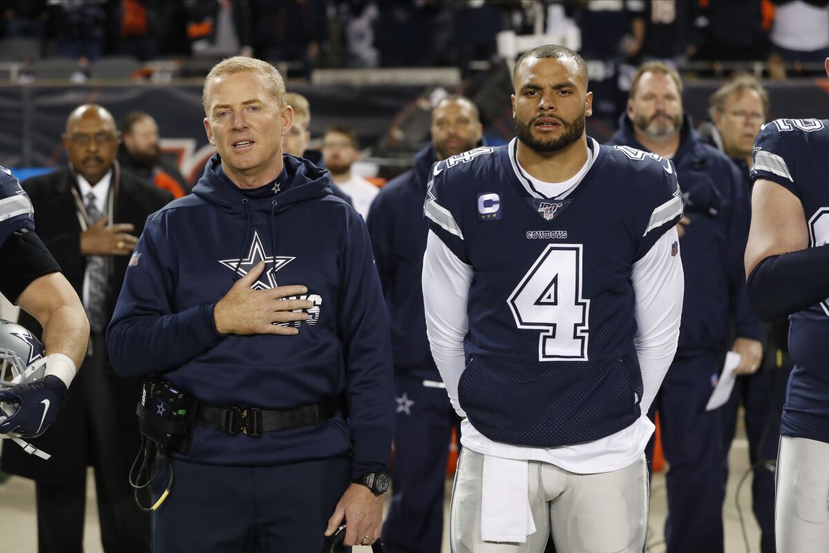 FILE - In this Dec. 5, 2019, file photo, Dallas Cowboys coach Jason Garrett and quarterback Dak Prescott (4) listen to the national anthem before the team's NFL football game against the Chicago Bears in Chicago. Prescott wants his teammates to decide for themselves whether to protest during the national anthem. Defensive lineman Tyrone Crawford says they have the “green light” to do so. Owner Jerry Jones hasn't said in so many words, but it appears his hard-line stance over his players standing during the anthem has eased amid a national reckoning over racial justice. (AP Photo/Charles Rex Arbogast, File)