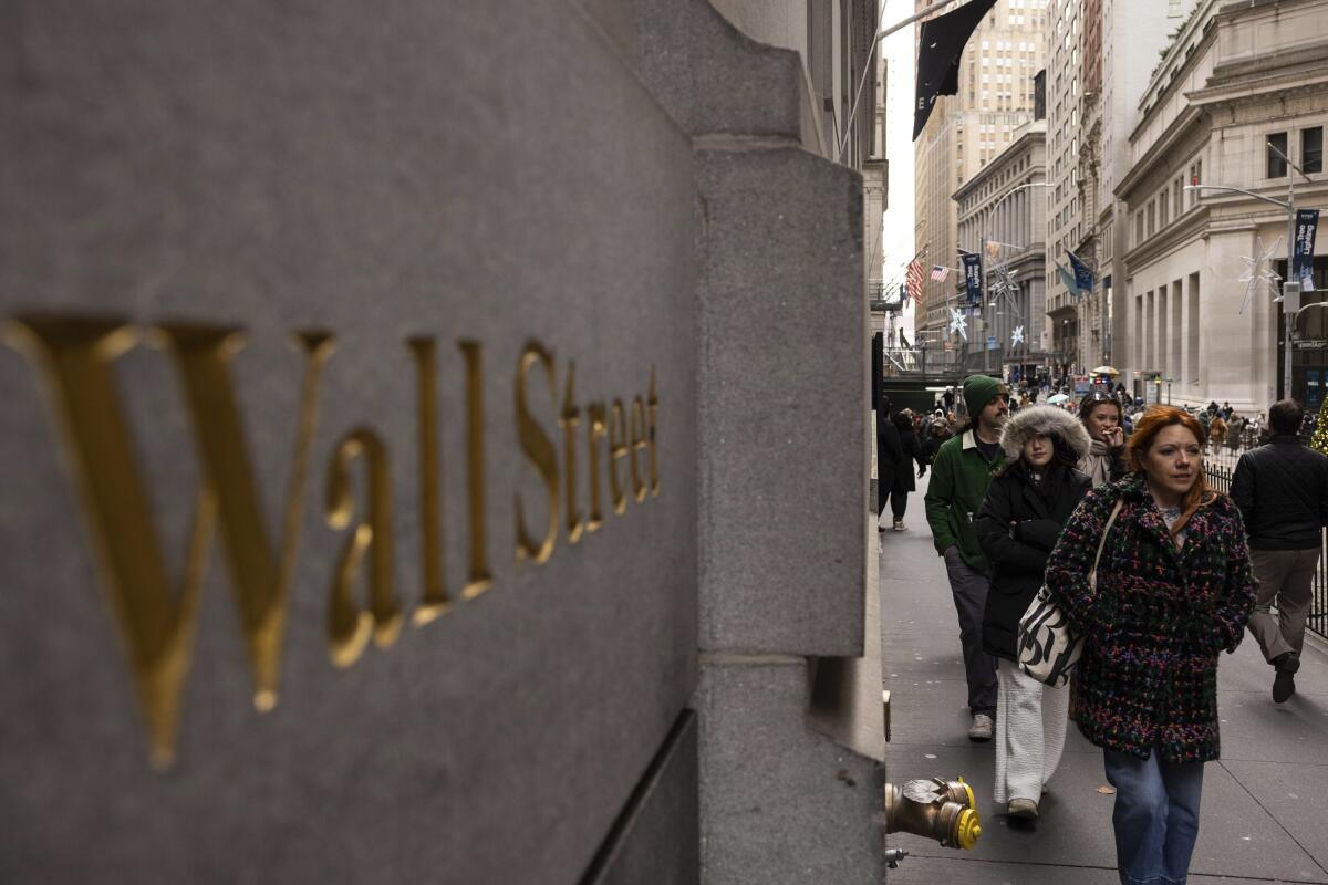 People walk past a Wall Street sign outside the New York Stock Exchange.