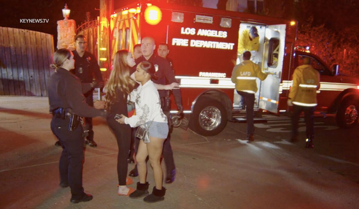 Police stand with people in casual clothes in front of a Los Angeles Fire Department vehicle at night.