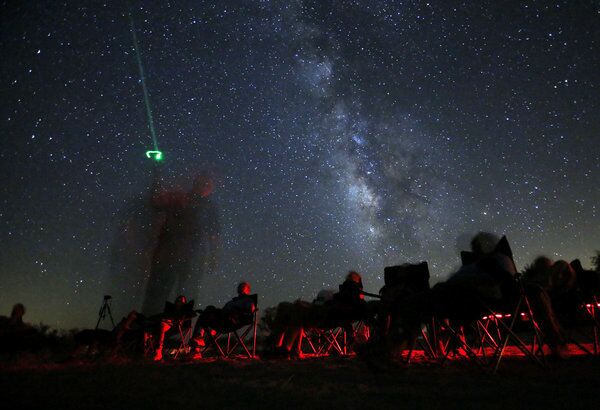 Stargazers on a tour with California Overland Desert relax on a dry lake bed in the Anza-Borrego Desert State Park and watch astronomer writer and photographer Dennis Mammana use a green lazer to point out objects in the night sky.