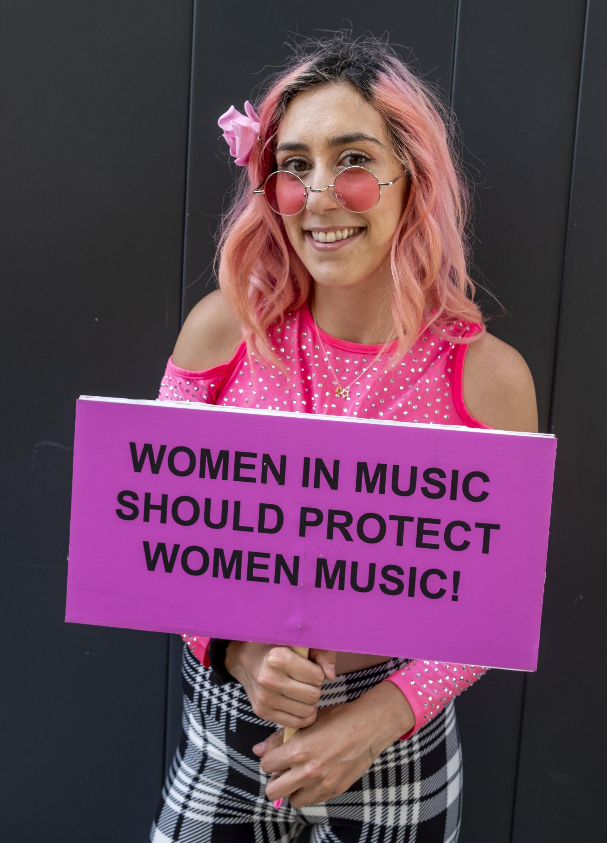 A woman holds a sign that reads "Women in music should protect women music"