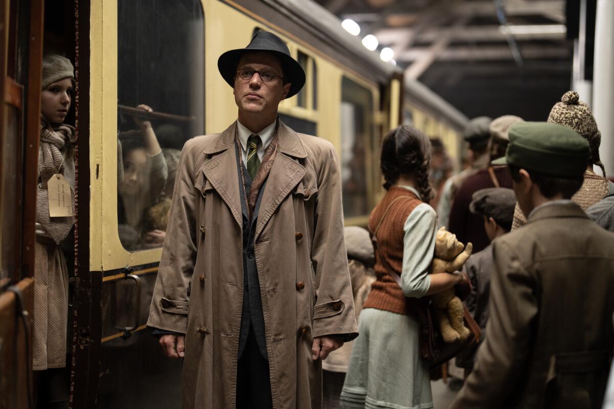 A man in a trench coat walks past a train.