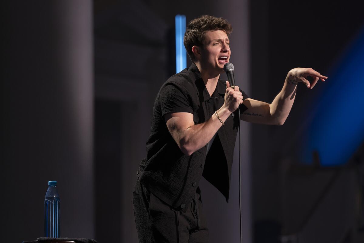 Comic Matt Rife pointing a finger as he performs stand-up comedy onstage in a black shirt and black pants