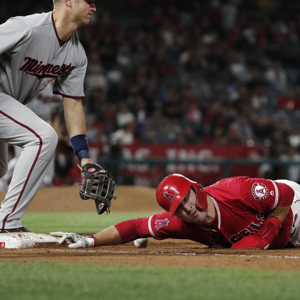 Angels center fielder Mike Trout (27) dives safely back to first base despite being hit by the throw from Minnesota Twins starting pitcher Jose Berrios (17) as Minnesota Twins first baseman Joe Mauer (7) couldn't reach the ball in the fifth inning at Angel Stadium on May 10, 2018.