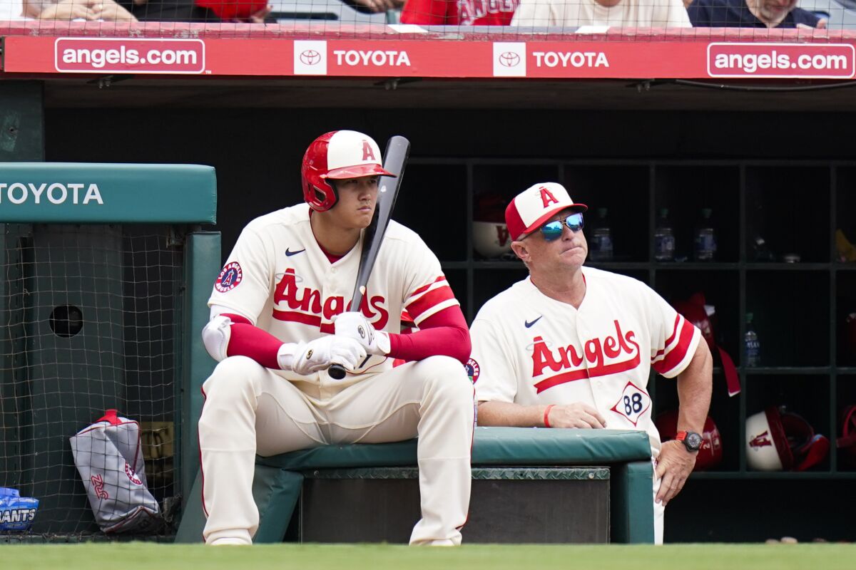Angels' Shohei Ohtani sits on a box near interim manager Phil Nevin.
