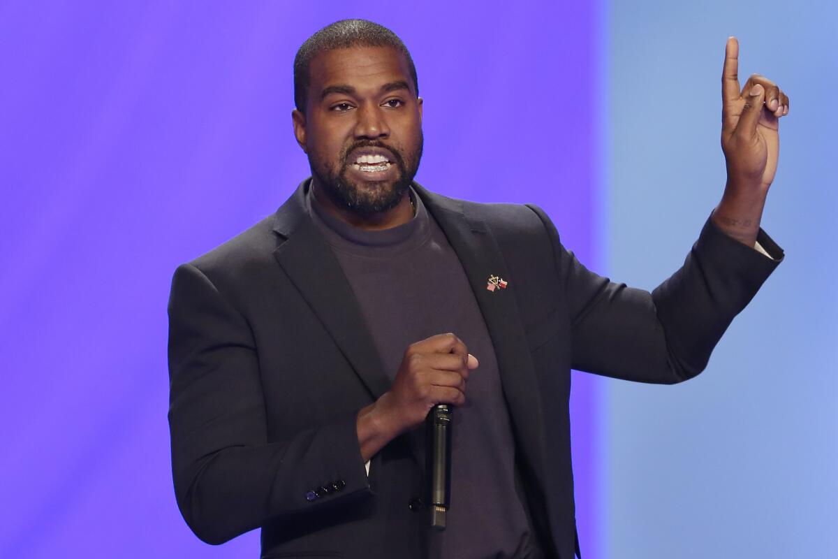 Kanye West speaks into a microphone while pointing upward