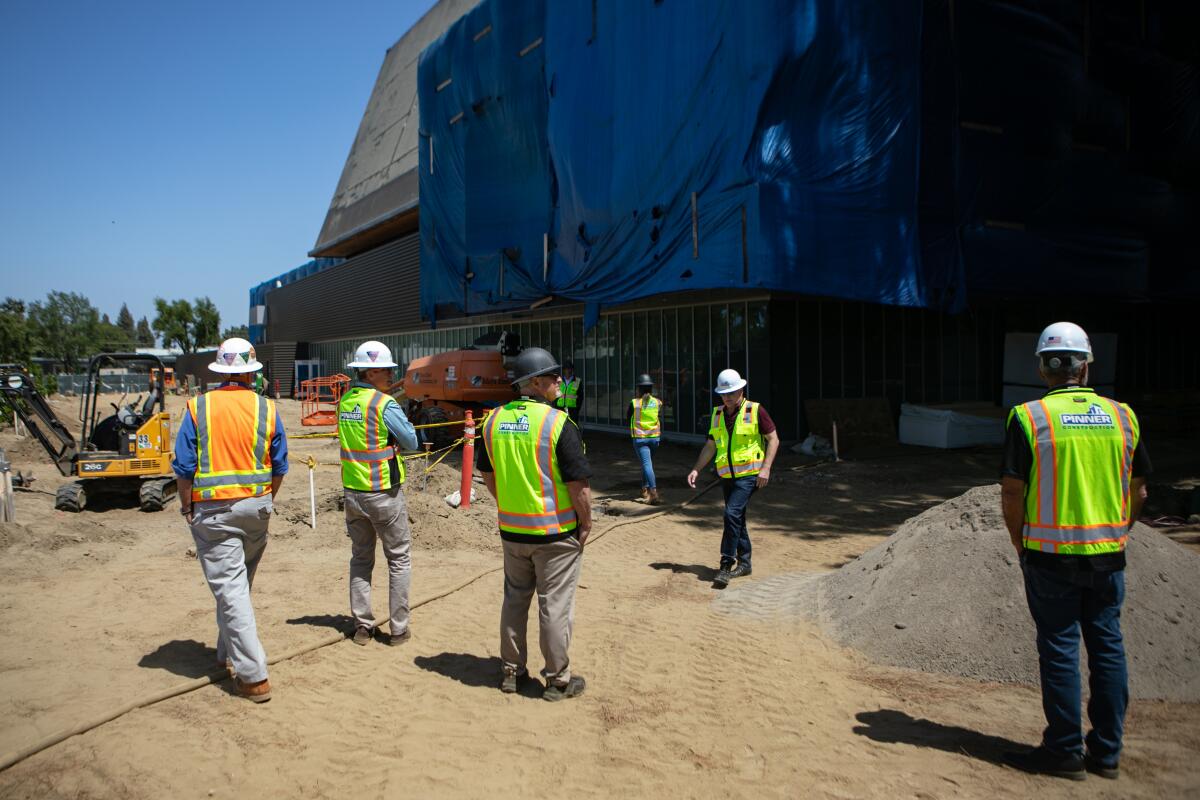 People in yellow or orange vests stand outside in a construction site.