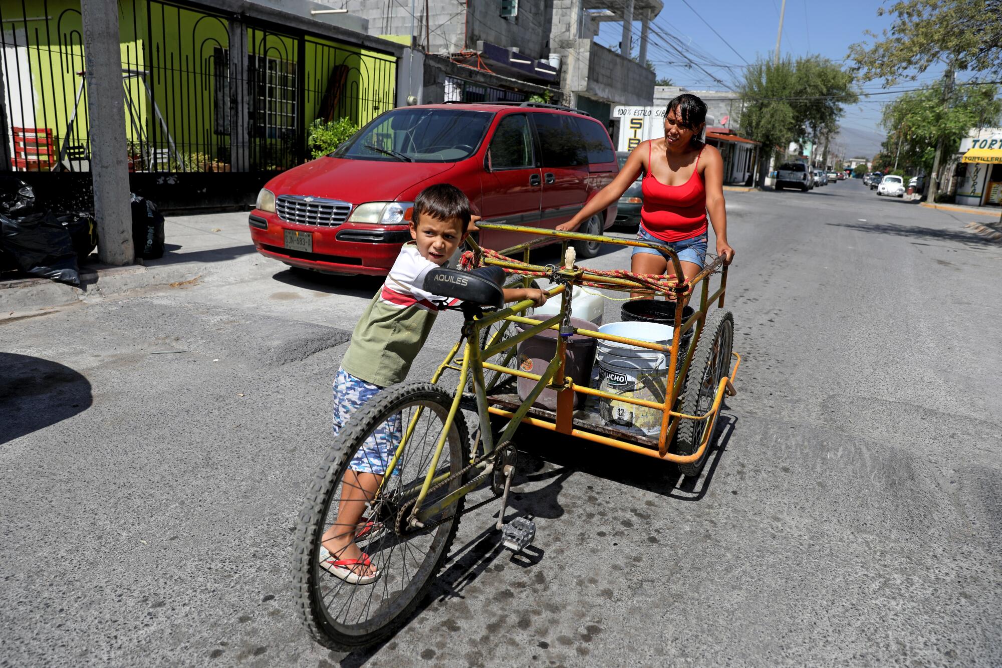 A woman and young boy with a tricycle cart carrying water buckets