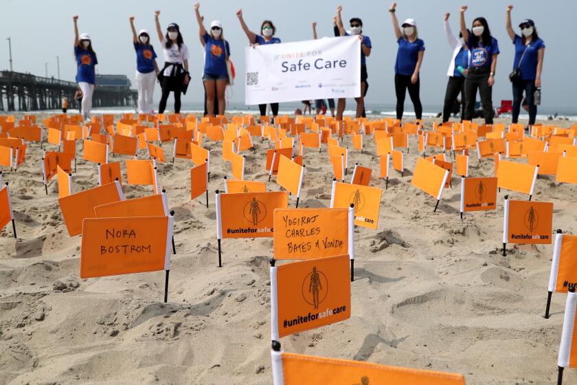 Patient Safety Movement Foundation members raise their fists in solidarity for those who died from preventable medical errors as they pose for group photo on Tuesday morning at Newport Pier in Newport Beach. The names of patients Nora Bostrom and Yogiraj Charles Bates are written on flags planted in the sand. Vonda Bates, still living, is a foundation board member who is the widow of Yogiraf Charles Bates.